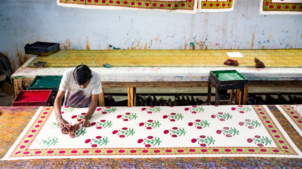 indian block print textiles are placed upon a long table to enable the indian printer to create uniquely complex designs