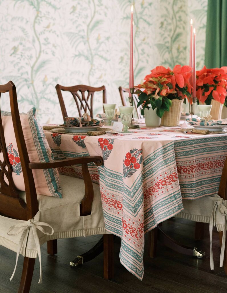 Ambiance of lit holiday candles over a traditional holiday tablescape with a Indian block print tablecloth, flowers.