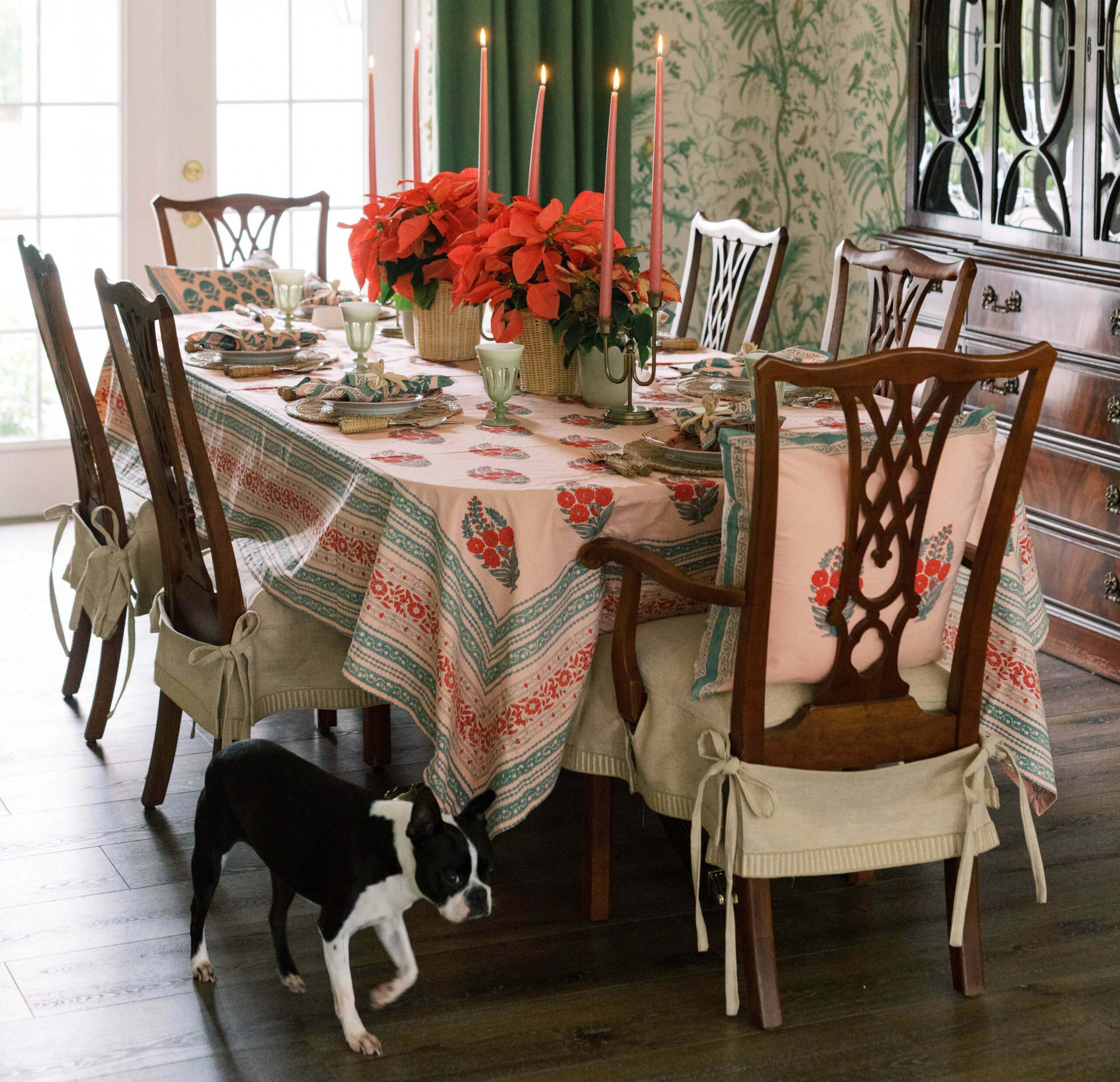 Full view of a holiday dining table setting. ready for a holiday party, covered by a traditional Pink Indian block print table cloth with floral motifs.