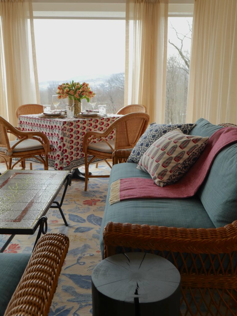 Sunroom with our Hana block printed tablecloth and napkins with blue and red florals, and Lotus-Yasmin block printed reversible pillow covers showcasing classic Indian block prints on Swedish, mid-century modern furniture.