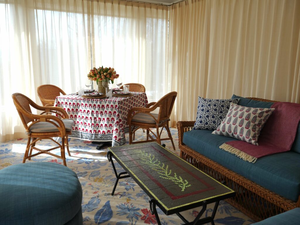 Sunroom with our Hana block printed tablecloth and napkins with blue and red florals, and Lotus-Yasmin block printed reversible pillow covers showcasing classic Indian block prints on Swedish, mid-century modern furniture.